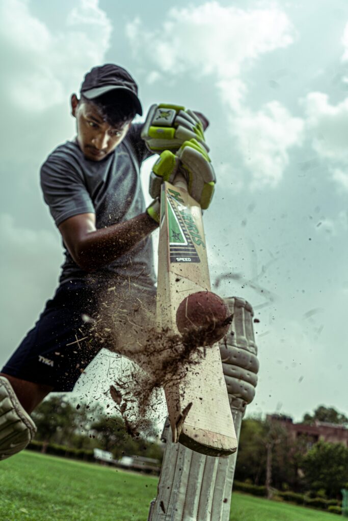 Young cricket batsman playing an explosive shot, ball striking the bat with dirt flying on a practice ground